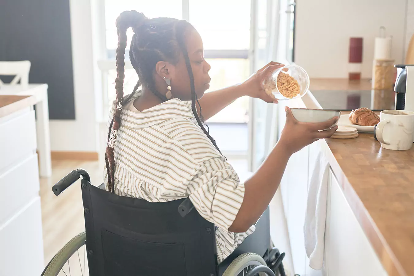 A disabled woman sitting in her wheelchair putting cereal in her bowl